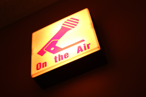 Glowing sign that reads On The Air and shows a microphone