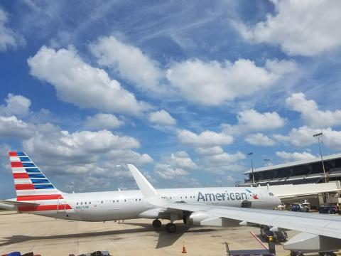 An American Airlines plane parked at the gate at an airport against a blue sky with many white clouds