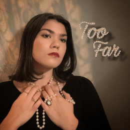 Girl wearing black top and pearl necklace has hands on neck while looking forward