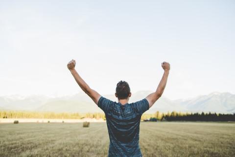 Shown from behind, guy outdoors with both arms raised