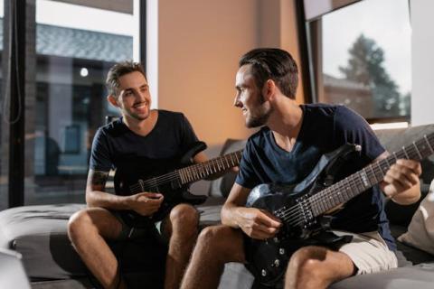 Two young men holding guitars seated next to each other on a couch Two young men holding guitars seated next to each other on a couch