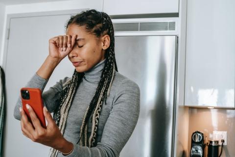 Female with fist to forehead and holding smartphone