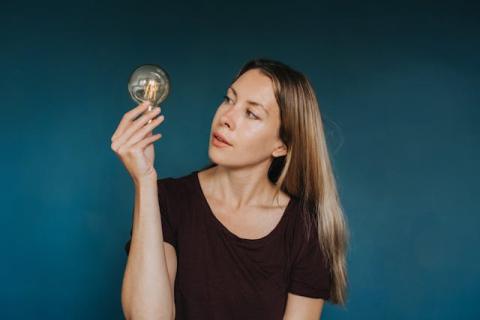 Girl turning head almost sideways to look at a light bulb she's holding up Girl turning head almost sideways to look at a light bulb she's holding up