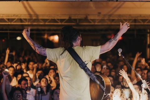 Performer shown from behind with arms raised looking at cheering crowd