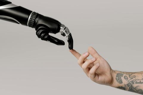The fingertip of a human arms touches the fingertip of a robotic arm