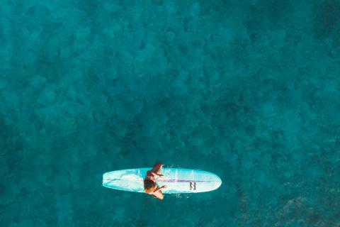 A female sits on a surfboard out on the open water with one leg over each side