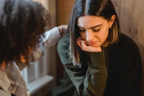 Disconsolate brunette with chin in hand gets a hand on her shoulder Disconsolate brunette with chin in hand gets a hand on her shoulder