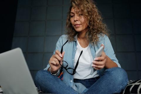 Curly-haired woman holding smartphone and reading from laptop