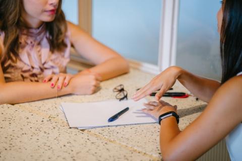 Two females, faces cropped out, sitting across from each other, talking Two females, faces cropped out, sitting across from each other, talking