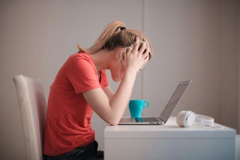 Side view of female seated with head in hands looking at laptop Side view of female seated with head in hands looking at laptop