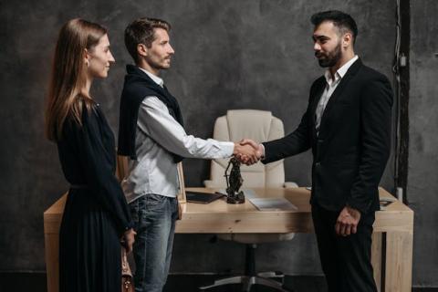 Two men shake hands while a woman stands alongside one of them Two men shake hands while a woman stands alongside one of them