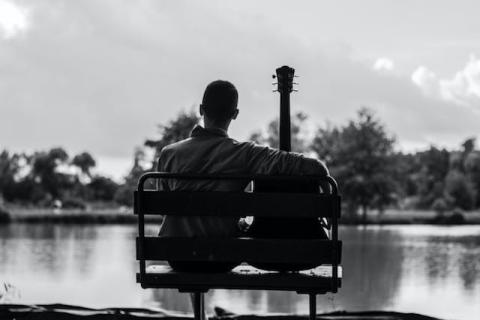 View from behind of guy sitting next to his guitar on a bench overlooking water View from behind of guy sitting next to his guitar on a bench overlooking water