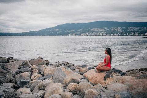 A girl sits cross-legged on rocks alongside a lake A girl sits cross-legged on rocks alongside a lake
