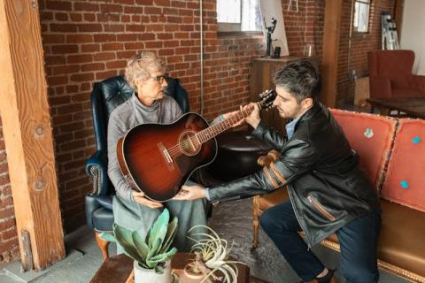 A middle aged man sits next to and helps a woman who is holding a guitar A middle aged man sits next to and helps a woman who is holding a guitar