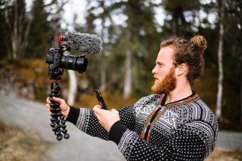 Profile of male holding camera in right hand and phone in the other